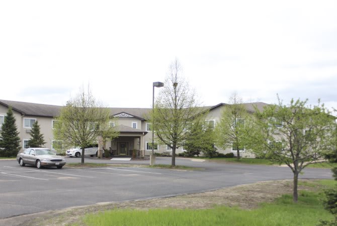 A view of a building with a parking lot and trees in the foreground under an overcast sky.