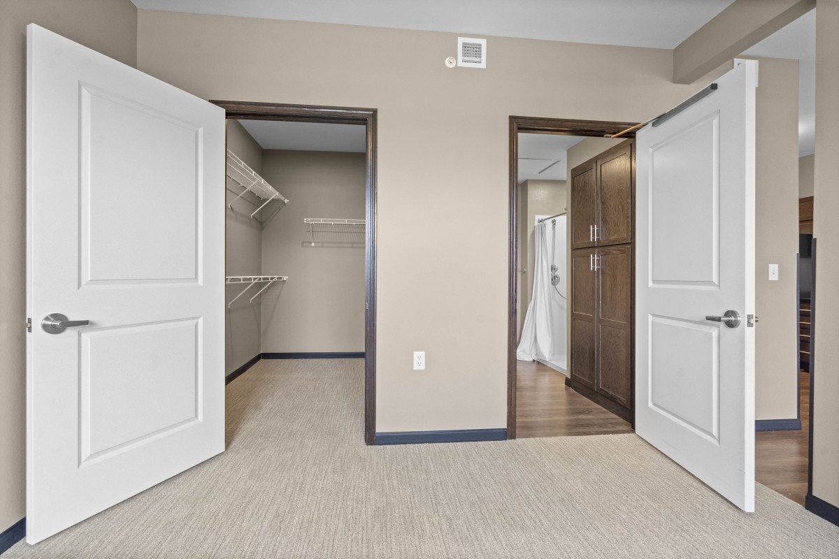 An empty room featuring open closet doors and neutral-colored walls.