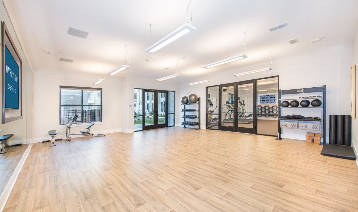 A spacious and modern yoga studio with bright lighting, wooden floors, and large windows.