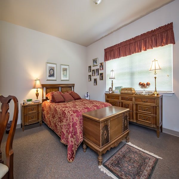 A cozy bedroom featuring wooden furniture, a bed with patterned bedding, and a window letting in natural light.