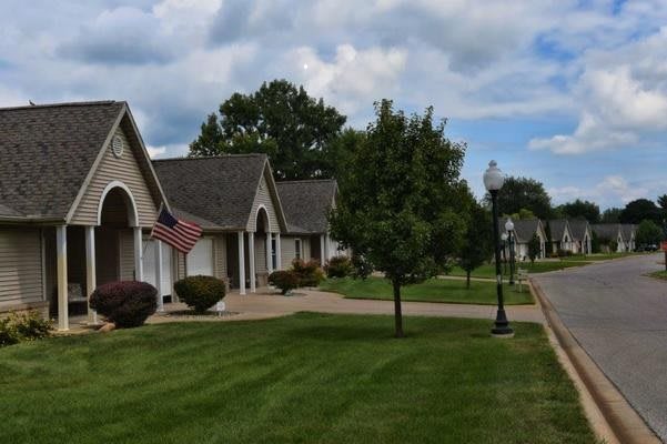 A quiet suburban street lined with houses and well-manicured lawns under a cloudy sky.