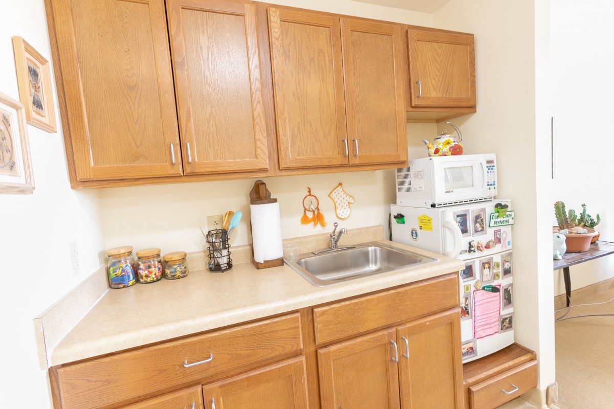 A cozy kitchen area featuring wooden cabinets, a countertop with storage jars, a sink, and a microwave.