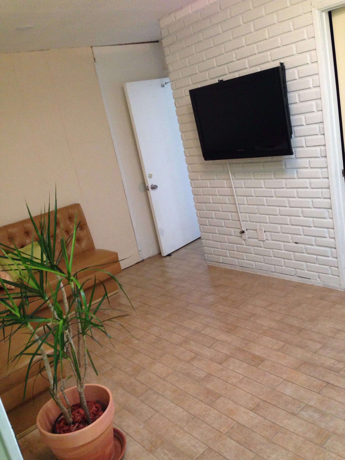 A cozy living room with a television on a brick wall, a plant, and a sofa.