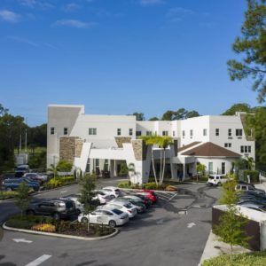 A modern building with a parking lot surrounded by trees on a clear day.