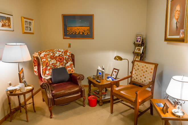 A cozy corner of a living room featuring two chairs, a small table with framed pictures, and a lamp.