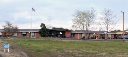 A view of a single-story brick building surrounded by grass and trees.