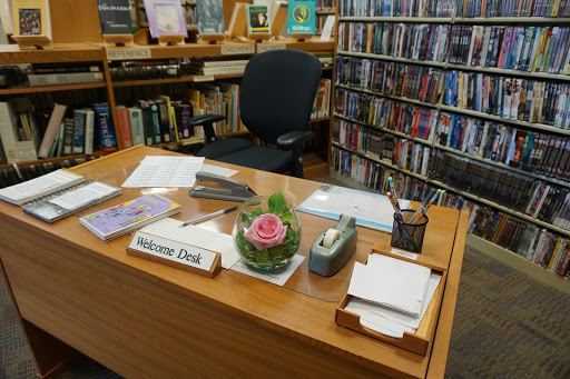 A neatly organized desk in a library, featuring stationery and a decorative flower arrangement.