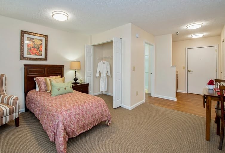 A cozy bedroom with a single bed, nightstand, and an open closet displaying a robe.