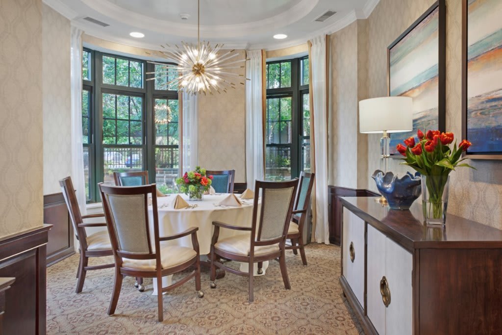 A well-lit dining room featuring a round table with chairs, a modern chandelier, and large windows.