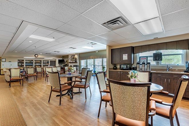 A spacious dining area with tables and chairs, featuring a wooden floor and large windows for natural light.