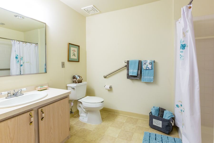 A tidy bathroom featuring a toilet, sink, mirror, and neatly arranged towels.
