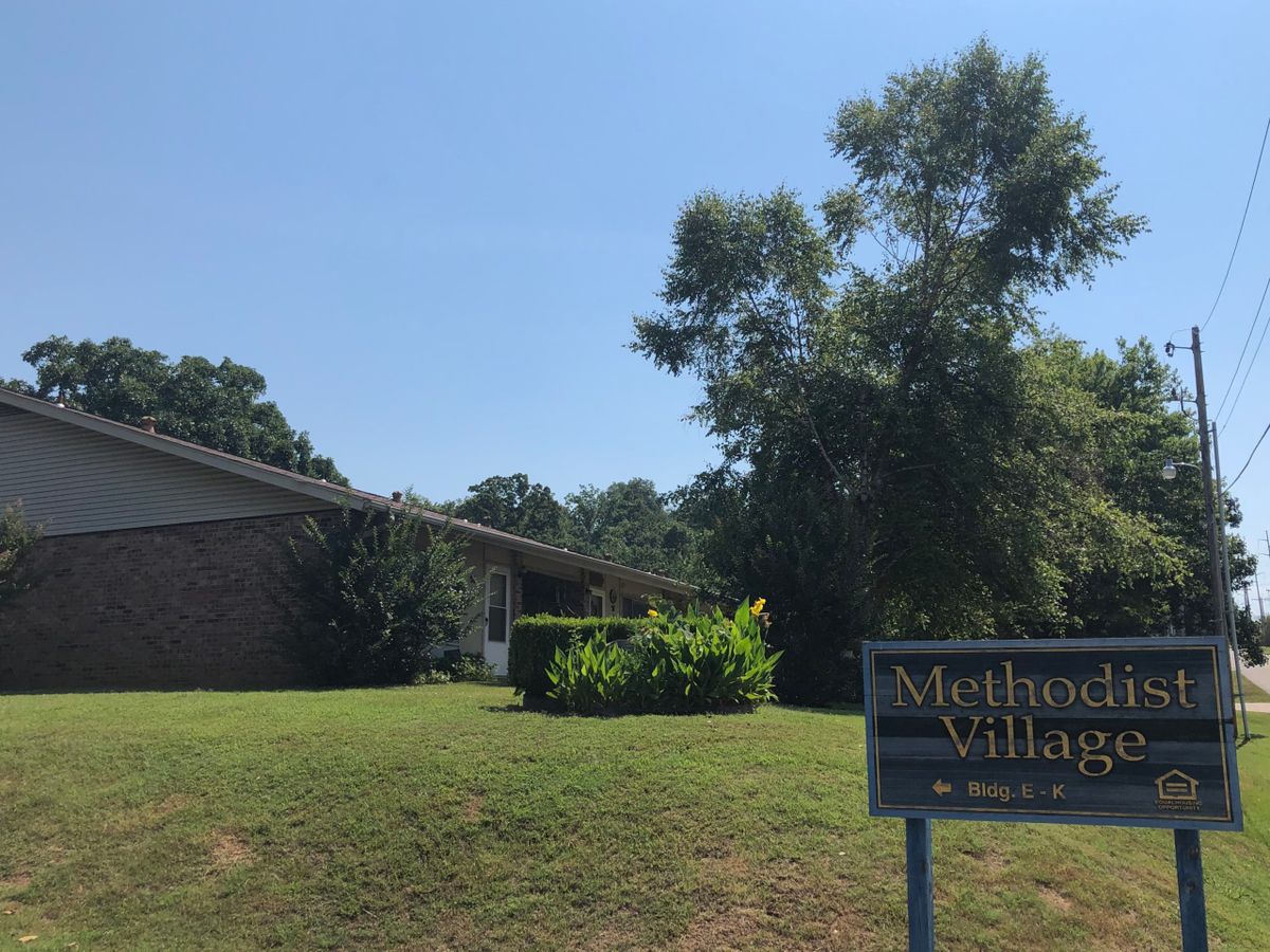 A building surrounded by trees with a sign on the lawn.