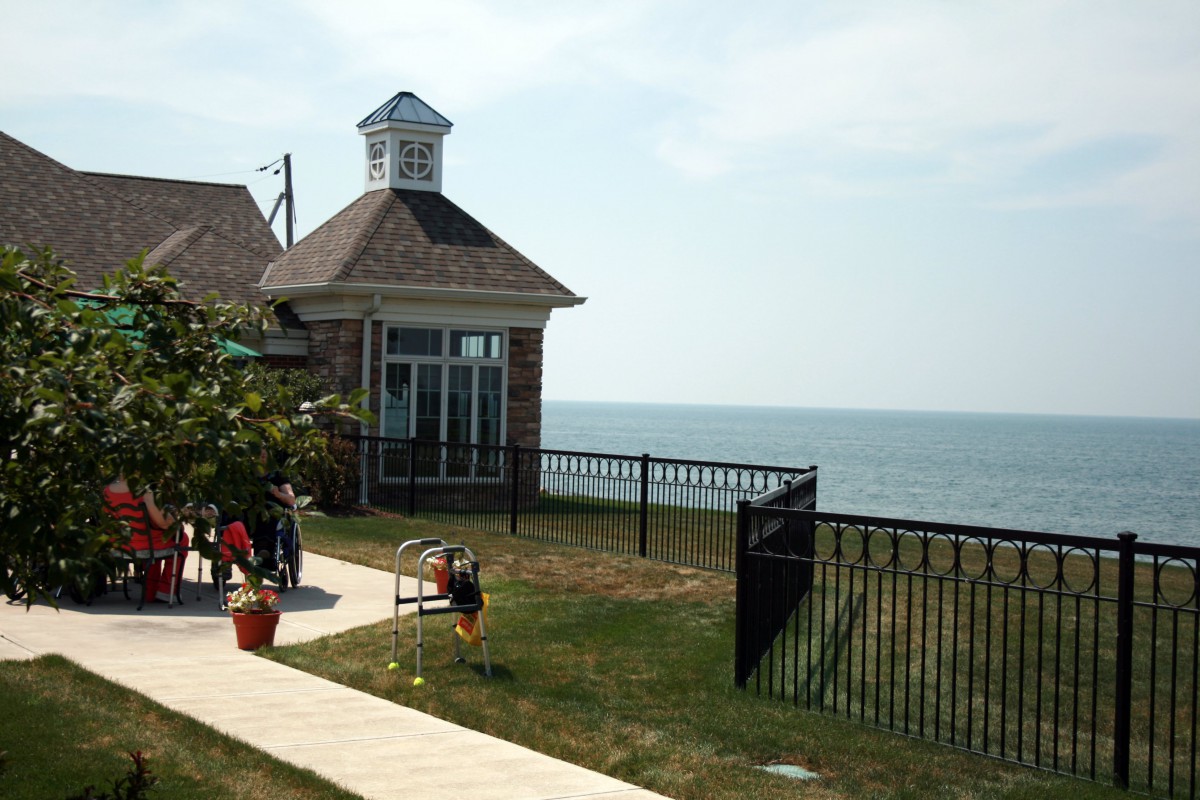 A coastal building with a view of the sea, surrounded by a fence and lawn where children are playing.