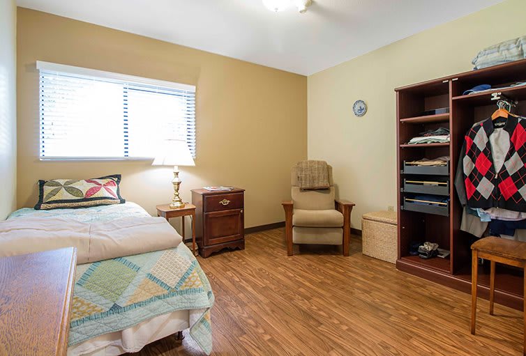 A cozy bedroom with a single bed, armchair, and wooden flooring.