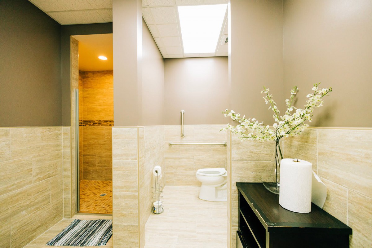 A modern bathroom with light-colored tiles, featuring a toilet, shower area, and decorative elements.