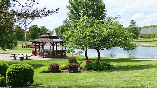 A serene park scene featuring a gazebo beside a tranquil lake, surrounded by lush greenery.