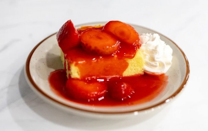 A slice of cake topped with fresh strawberries and drizzled with strawberry sauce, served with a dollop of whipped cream.