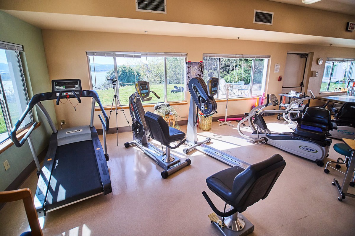 A well-equipped gym with various exercise machines and bright natural lighting.