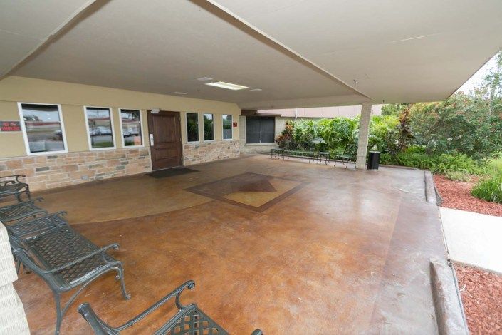 A spacious covered patio with seating and an entrance, surrounded by greenery.