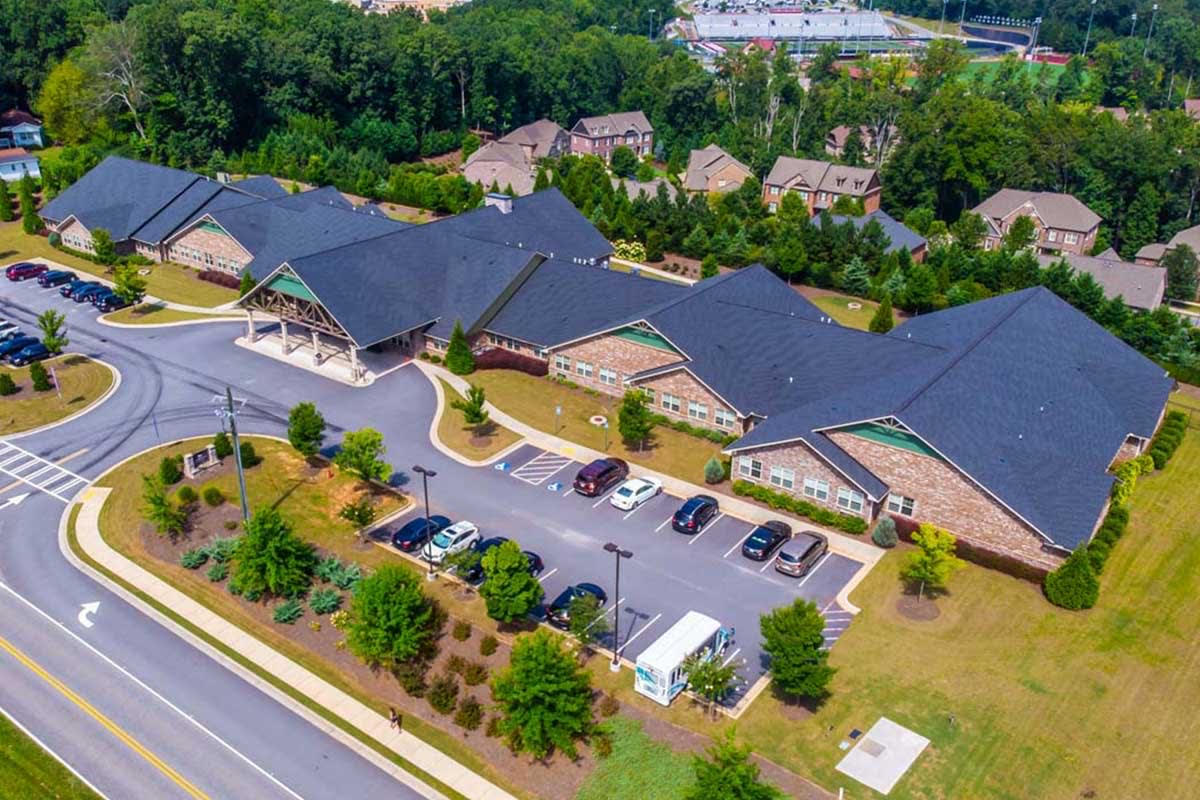 An aerial view of a building complex surrounded by greenery with a parking lot in the foreground.