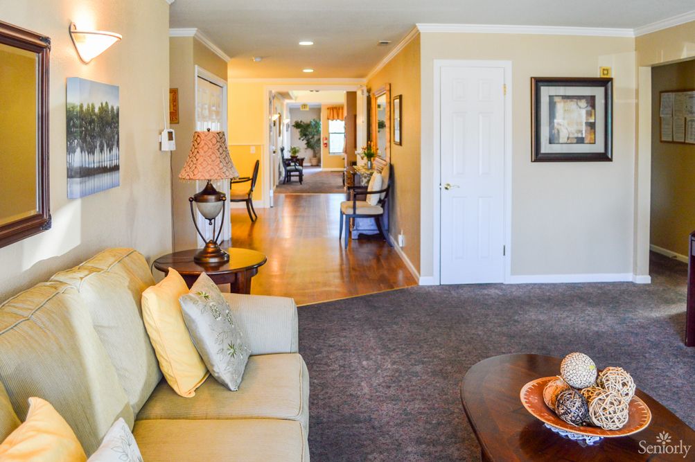 A cozy living room with a sofa, lamp, and decor leading into a hallway.