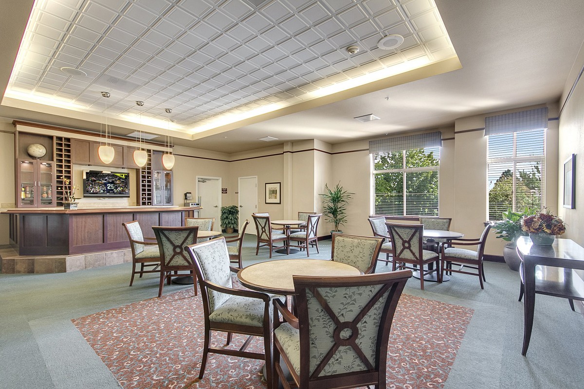 A spacious lounge area with tables and chairs, featuring a bar counter and large windows.