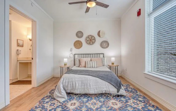 A cozy bedroom featuring a neatly made bed with decorative pillows, wall art above the headboard, and a patterned rug.