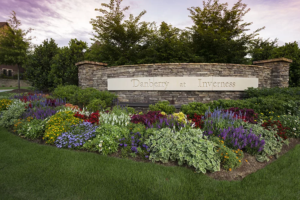 A beautifully landscaped garden with vibrant flowers in front of a stone wall containing signage.