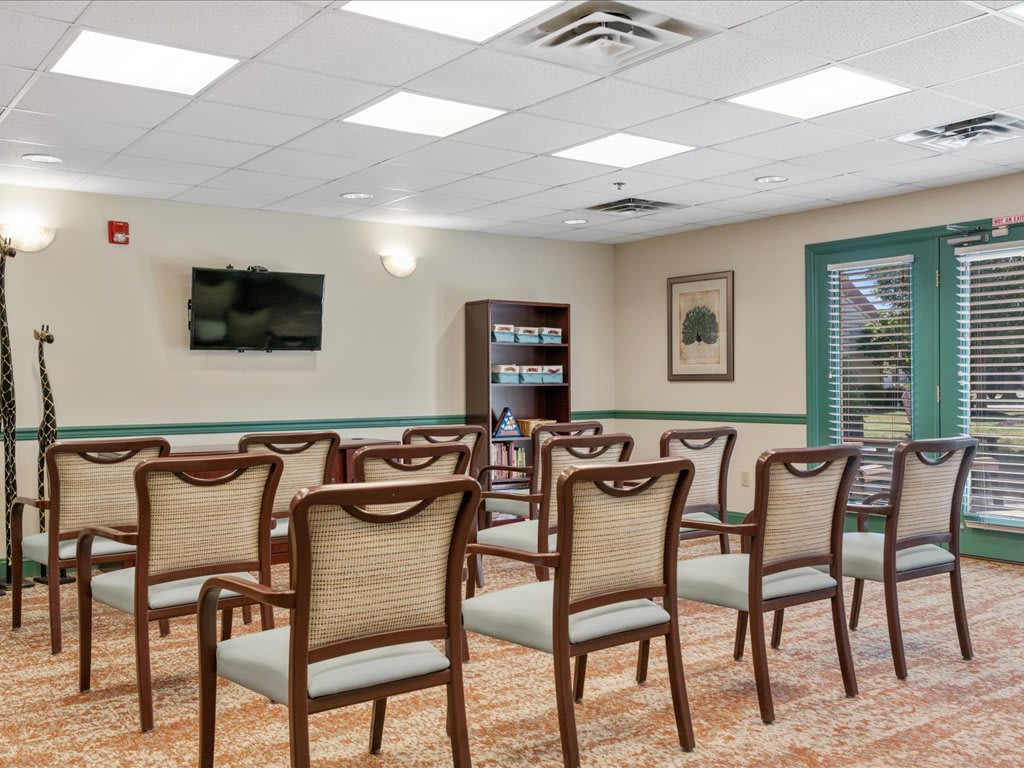 A neatly arranged conference room with chairs set up for a meeting, featuring a television and bookshelf.
