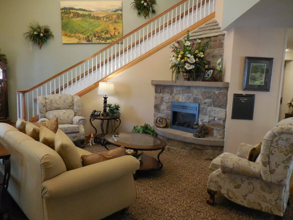 A cozy living room with a seating area, fireplace, and a staircase adorned with a decorative painting.