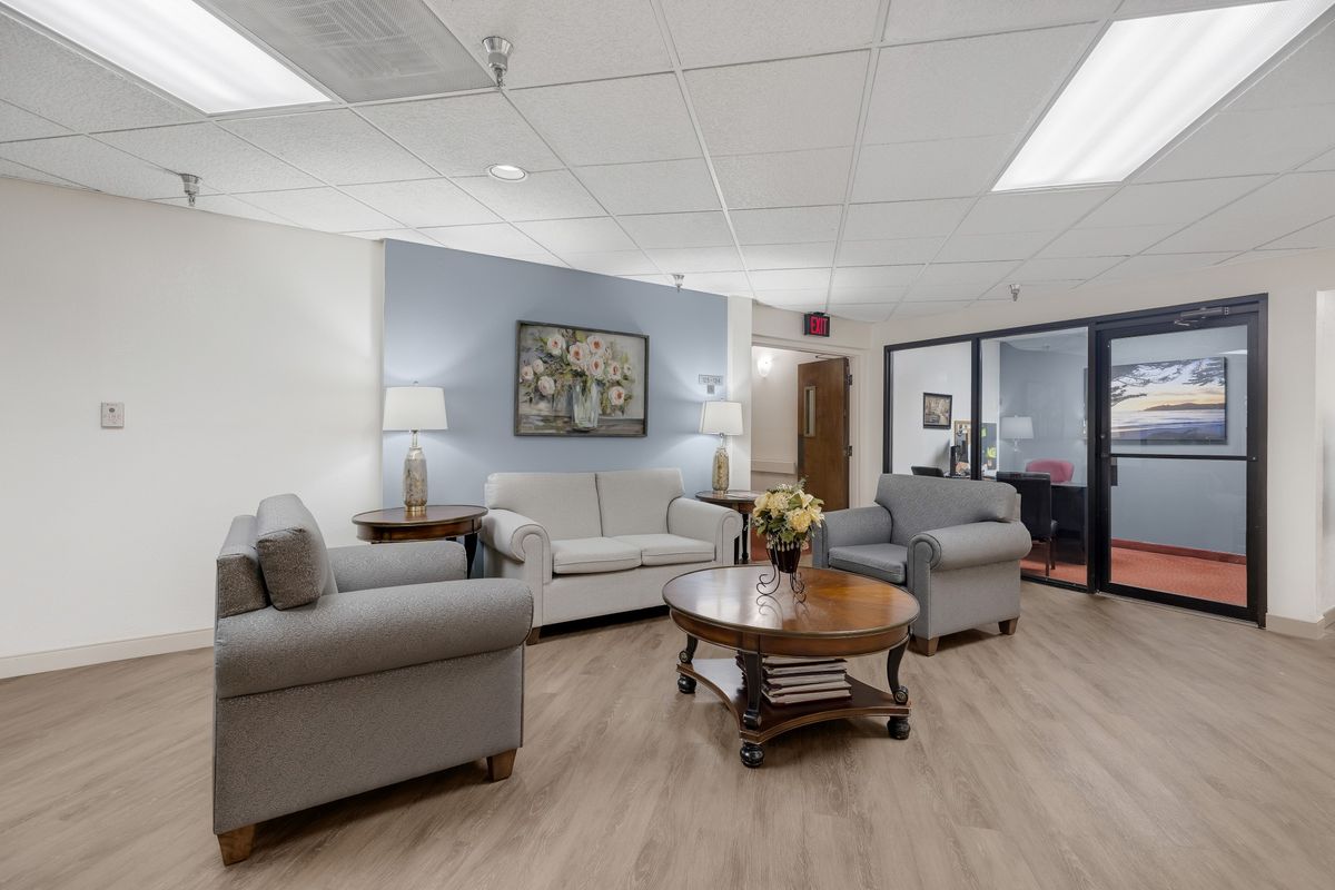 A comfortable waiting area featuring sofas, armchairs, a coffee table, and decor elements like lamps and artwork.