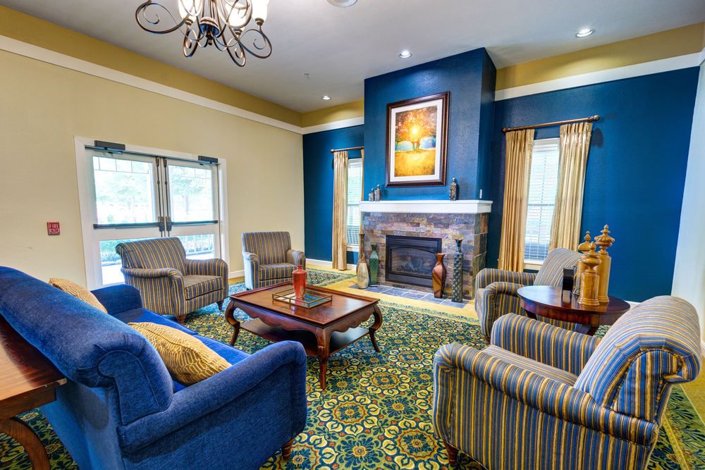 A cozy living room with a fireplace, featuring blue and yellow decor, comfortable armchairs, and a chandelier.