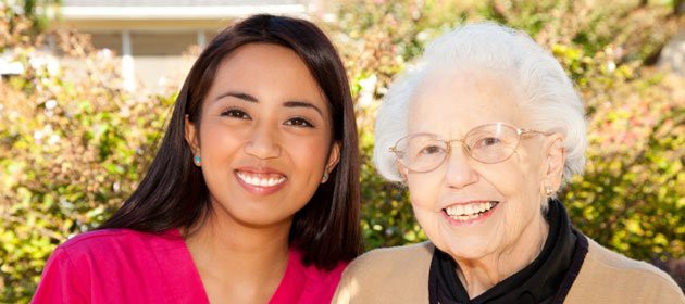 A younger woman and an elderly woman smiling together outdoors.