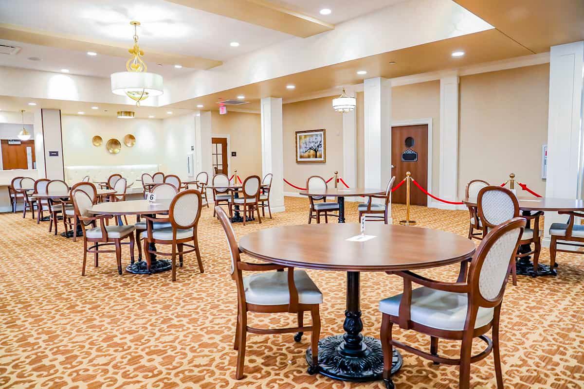 An elegant dining area featuring round tables and upholstered chairs, illuminated by chandeliers.