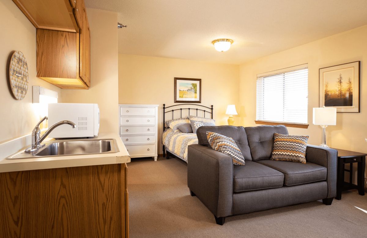 A cozy studio apartment featuring a bed, sofa, and kitchenette.