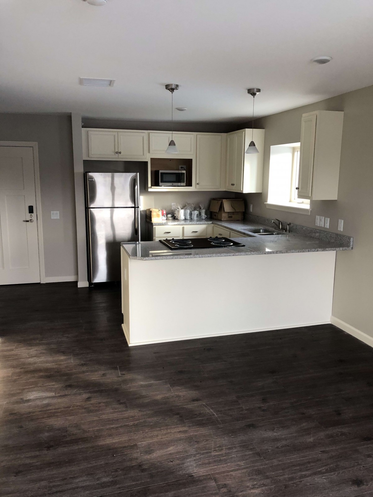A modern kitchen with stainless steel appliances and wood flooring in an open layout apartment.