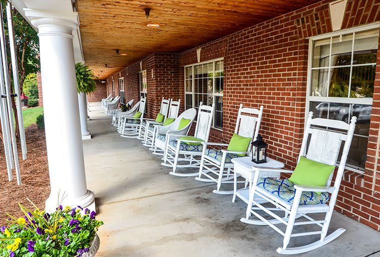 A charming porch lined with white rocking chairs adorned with green cushions and lanterns, set against a brick wall.
