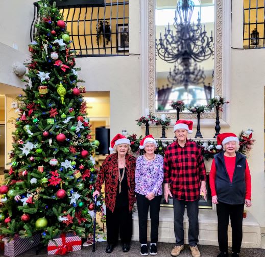 A group of people wearing Santa hats stand in front of a decorated Christmas tree, celebrating the holiday season.