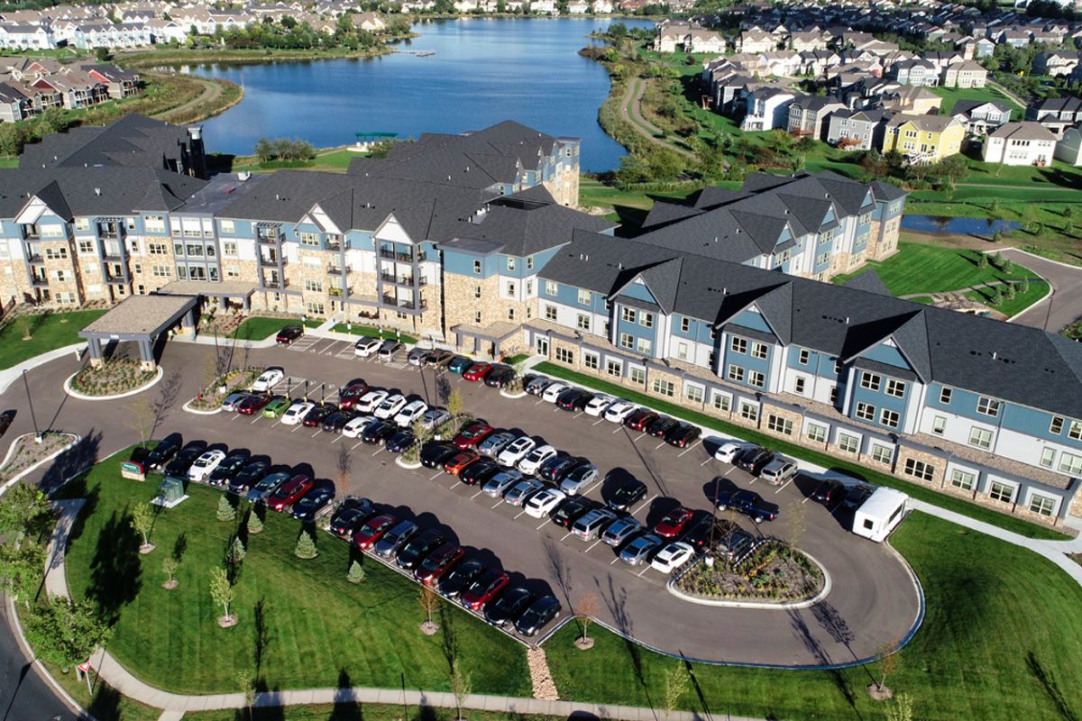 Aerial view of a residential building with a parking lot and nearby lake.