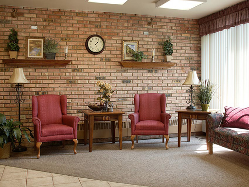 A cozy waiting area featuring red armchairs, wooden furniture, and decorative elements against a brick wall.