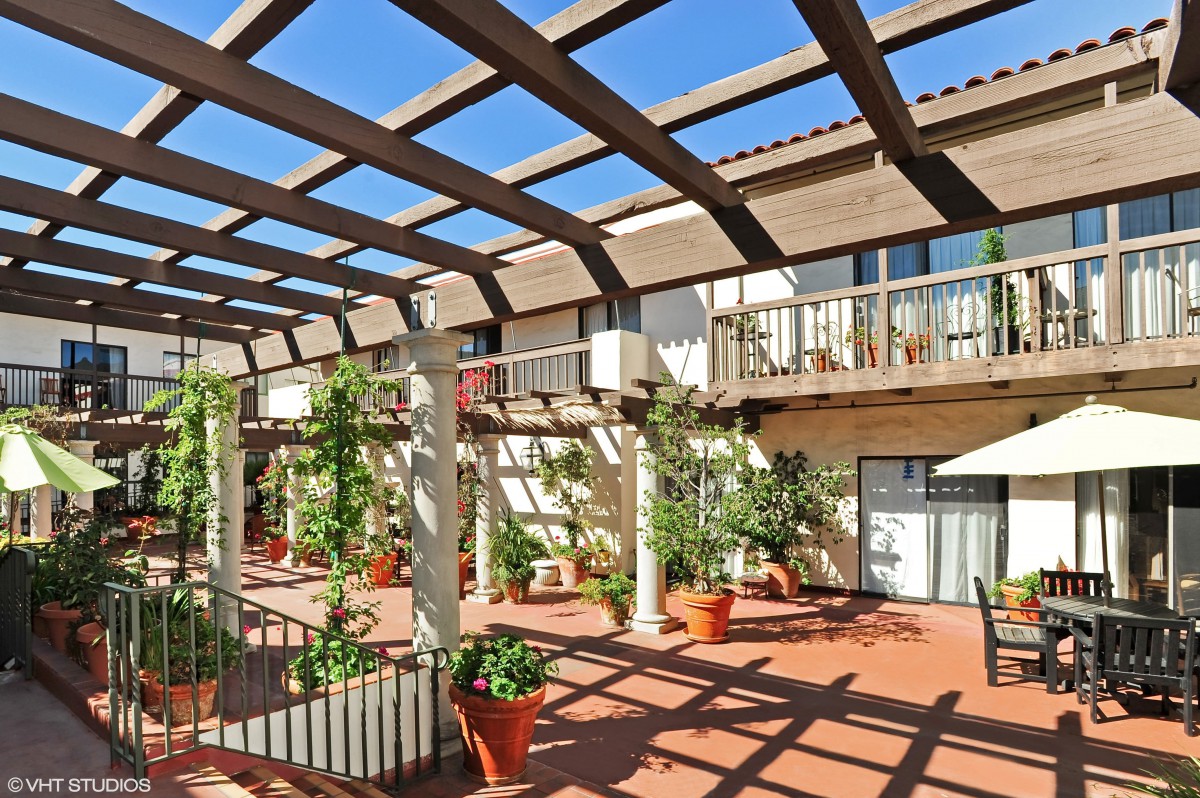 A sunny terrace with a wooden pergola and potted plants.