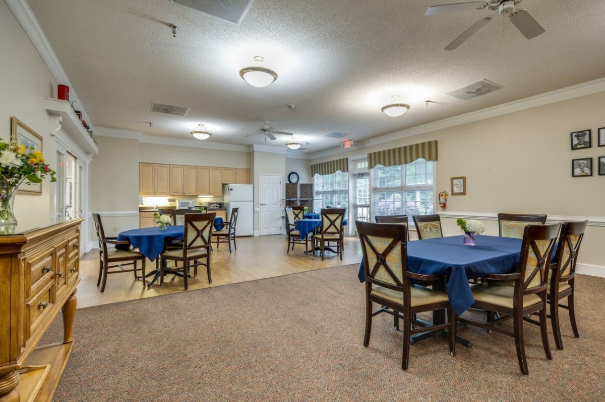 A welcoming dining area with multiple tables and chairs, adjacent to a kitchen in a community setting.