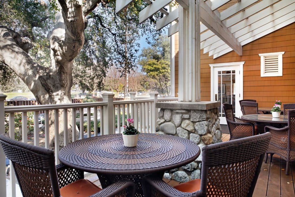 A cozy outdoor patio with a round table and chairs, surrounded by a wooden railing and stone accents.
