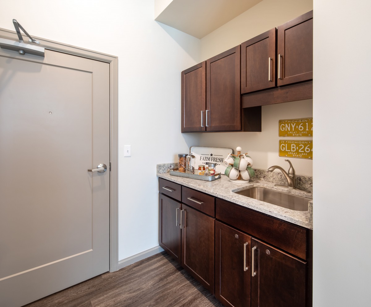 A compact kitchen area featuring dark cabinets, a countertop with a sink, and a door leading to another room.
