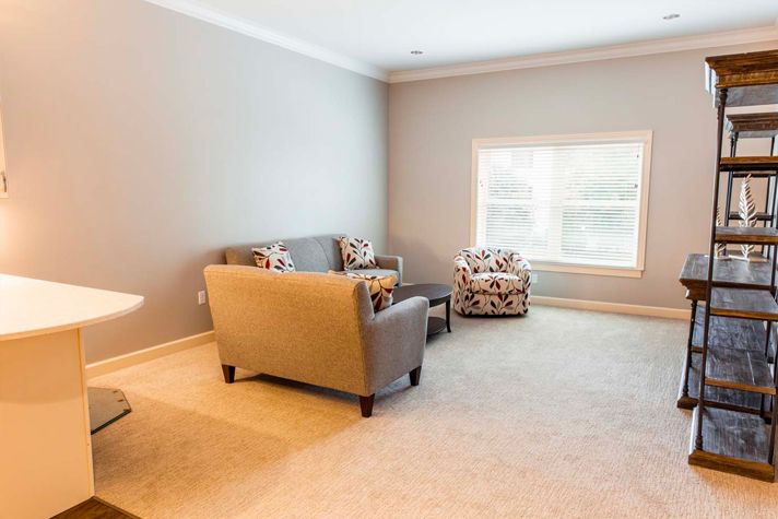 A bright and minimalist living room featuring a sofa, two patterned chairs, and large window.