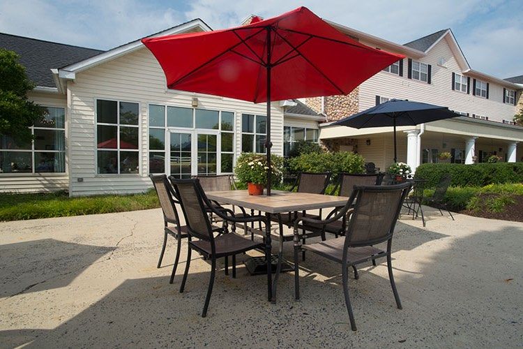 A sunny outdoor patio area with a table, chairs, and a red umbrella.
