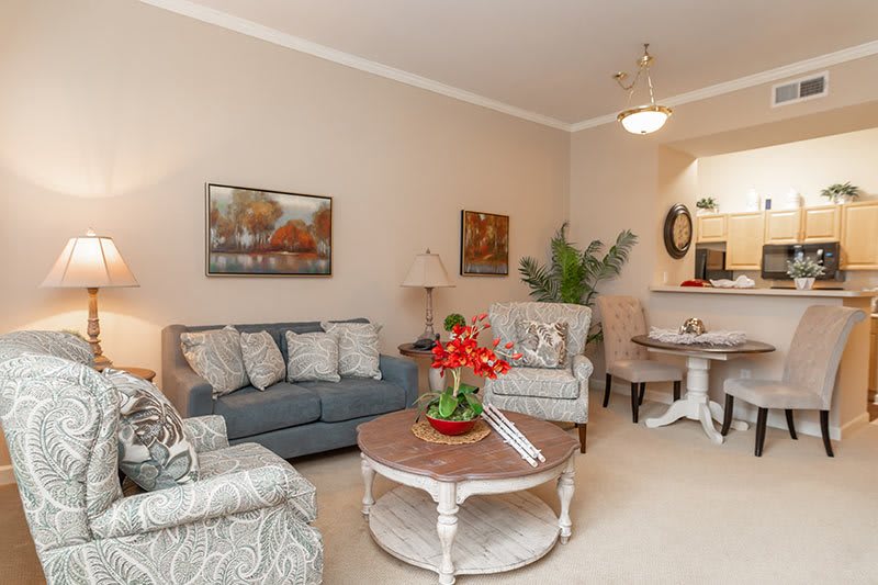A cozy living room with comfortable seating and tasteful decor, including artwork and indoor plants. Adjacent to the dining area, it features a sofa, chairs, coffee table, and lamps.