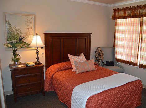 A cozy bedroom with a neatly made bed, wooden headboard, and a nightstand with a lamp.