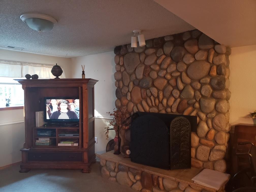 A cozy living room featuring a stone fireplace and an entertainment center with a television.
