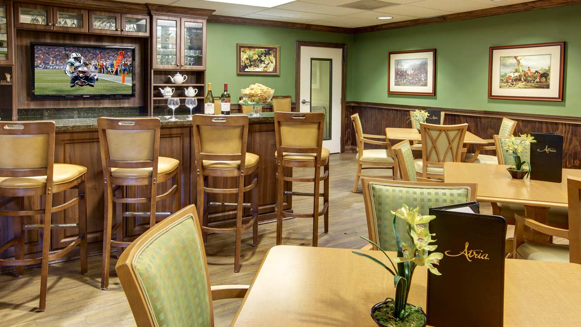 A cozy restaurant interior with a bar area, featuring green walls and neatly arranged wooden chairs and tables.